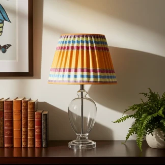 Ambientazione paralume. Lampada da tavolo classica con base in vetro e paralume artigianale a righe multicolore in un angolo lettura curato.