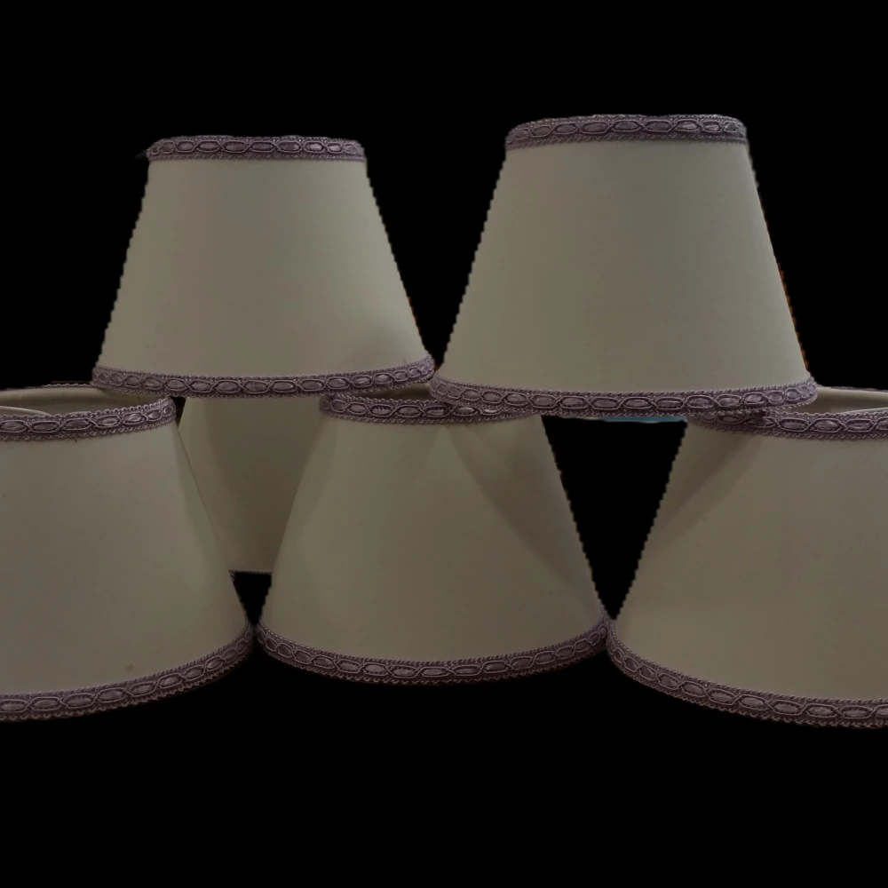 Set di Paralumi a Tronco di Cono in Cartapergamena con Passamaneria Violetto per Applique e Lampadari Paralumi a tronco di cono in cartapergamena color crema, impilati, rifiniti con passamaneria color violetto sui bordi superiore e inferiore, per applique o lampadari.