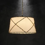 Paralume a sospensione tronco-conico realizzato in cartapergamena chiara, con decorazione esterna a intreccio creata da passamaneria scura.