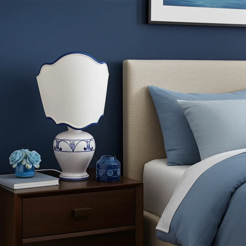 Paralume a Ventola Sagomato con Passamaneria Blu per Lampada da Tavolo Paralume a ventola con lati sagomati in tessuto avorio, rifinito con passamaneria blu, su una lampada da tavolo con base in ceramica bianca e blu