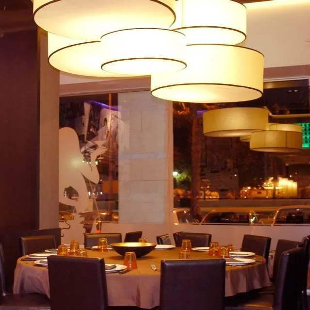 Composizione a Grappolo di Paralumi Cilindrici con Tappo Composizione a grappolo di paralumi cilindrici a soffitto, chiusi sul fondo, che illuminano la sala di un ristorante.