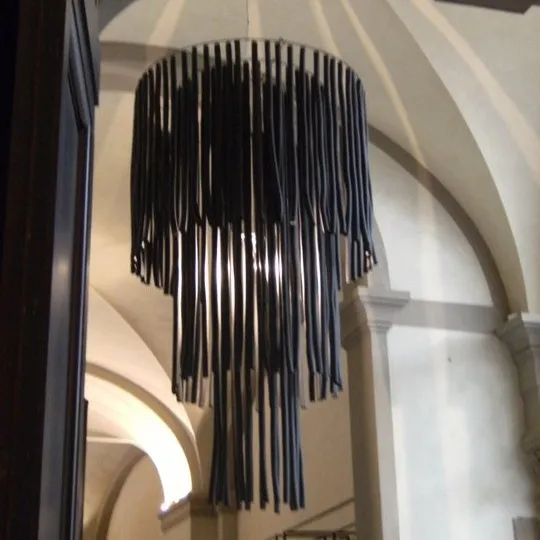 Paralume Scenografico Oversize in Materiale Plastico Lampadario/paralume scultoreo, alto circa 3 metri e largo 2 metri, realizzato con listelli di materiale plastico nero, all'ingresso di un palazzo storico.