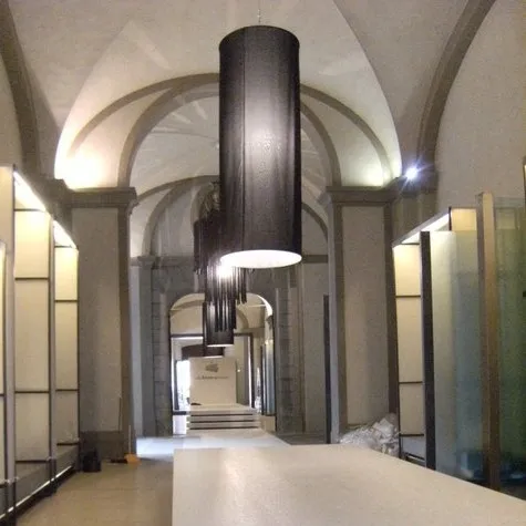 Paralumi Cilindrici Alti 3 Metri in Tessuto Nero per Passerelle di Moda Serie di paralumi cilindrici neri, alti circa 3 metri, appesi in un salone storico per illuminare una passerella di moda.