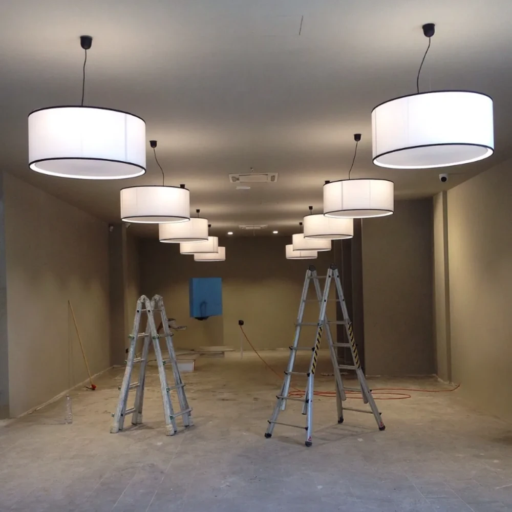 Paralumi Cilindrici con Tappo Diffusore . Illuminazione Negozio Grandi paralumi cilindrici a sospensione, realizzati in cartapergamena bianca e tappo diffusore inferiore, installati in un nuovo spazio commerciale ancora in fase di allestimento.