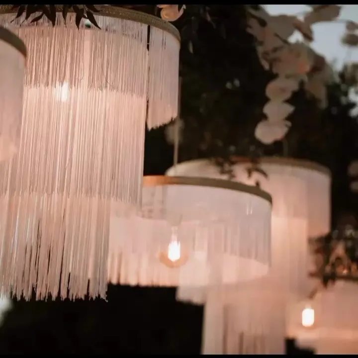Paralume Sospensione Matrimonio a Frange Stile Chandelier Paralumi a sospensione a più strati, realizzati con frange lunghe e bianche, che creano un effetto chandelier e illuminano un evento all'aperto o un tavolo nuziale.
