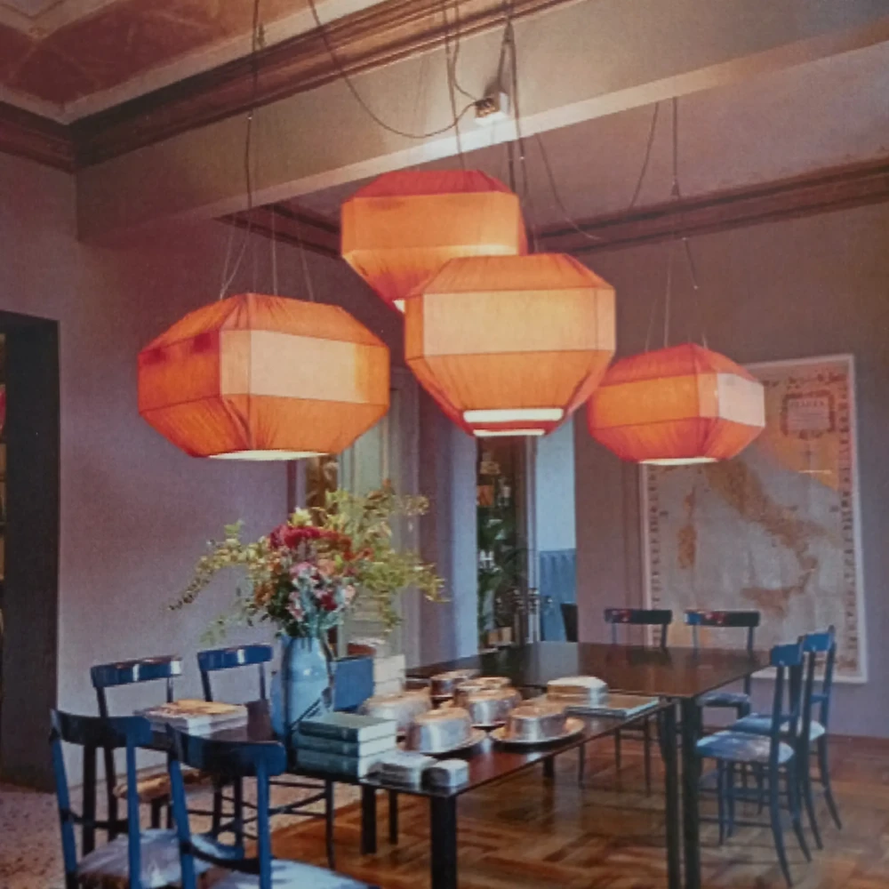 Paralumi a sospensione forma Ottagonale in Tessuto Arancione Gruppo di quattro paralumi a sospensione di grandi dimensioni, di forma ottagonale, in tessuto arancione, che ricordano delle lanterne, installati sopra un tavolo da pranzo.