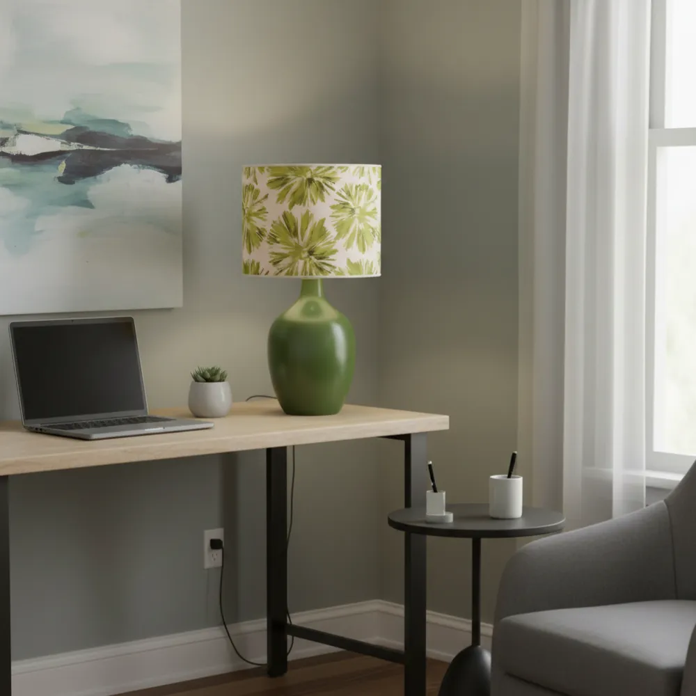 Paralume cilindrico con fiori verdi su lampada da tavolo coordinata in un ufficio moderno con scrivania in legno e laptop.Esempio di ambientazione