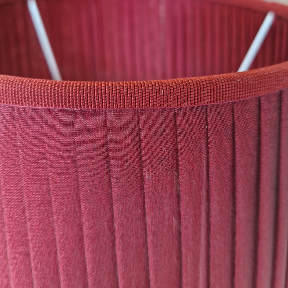 Dettaglio ravvicinato della lavorazione plissettata in organza bordeaux e finitura con passamaneria gros grain - Paralumi e Lumi Prato